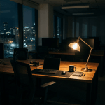 Office desk with laptop, lamp, coffee mug, notebook, and mouse at night